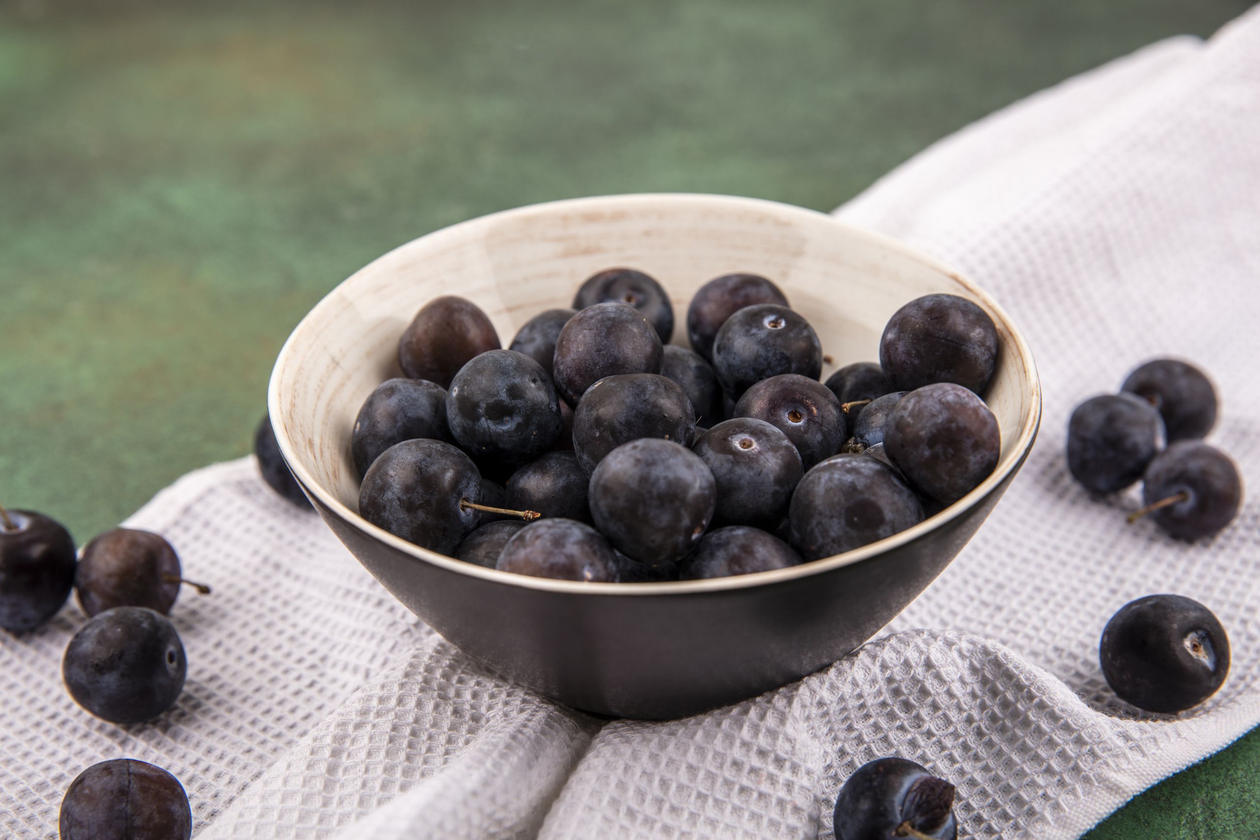 top view of the small sour blue-black fruit sloes on a bowl on white tablecloth on a green background
